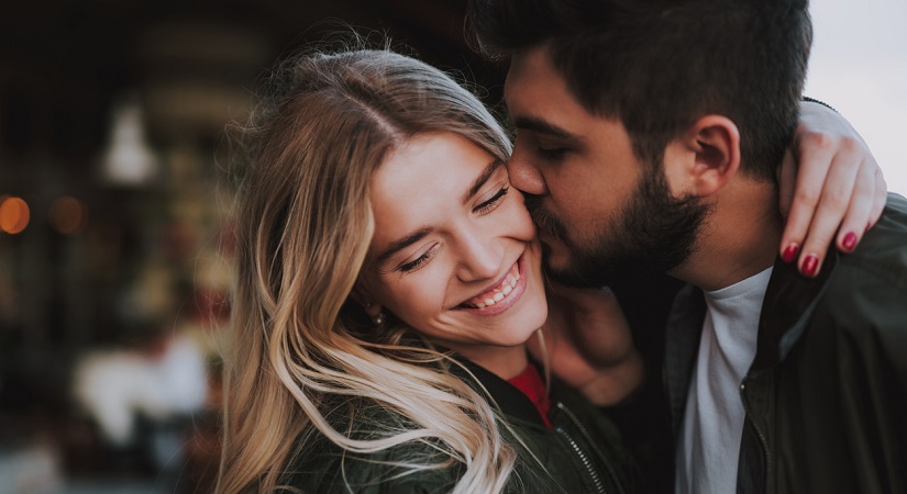 Precious moments of love. Close up portrait of handsome bearded guy kissing his girlfriend in cheek while she hugging him. Lady closing eyes with pleasure and smiling